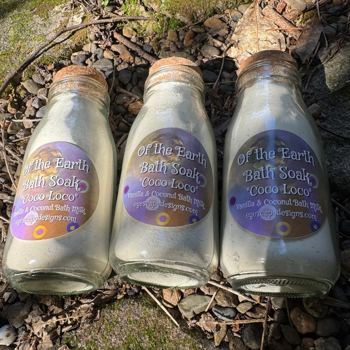 Three glass bottles labeled 'Of the Earth Bath Soaks Coco Loco' on a natural background.