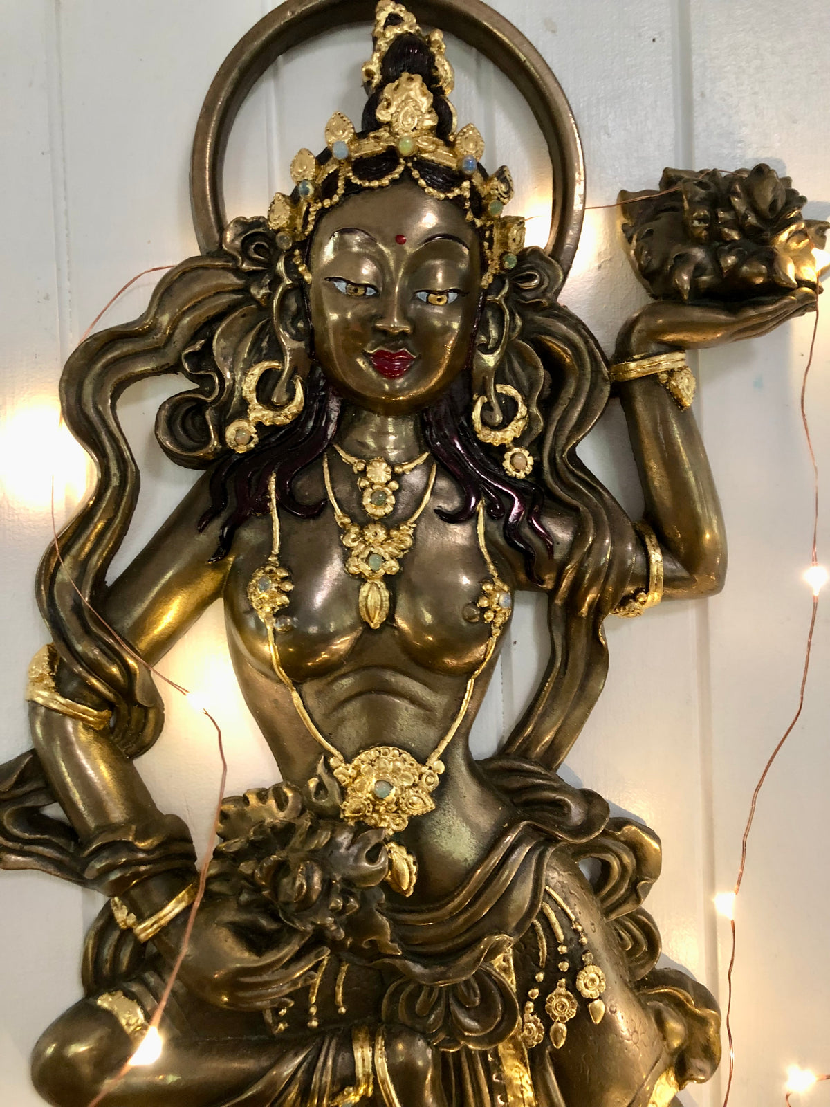 Polished bronze offering goddess close close up on a cream coloured wall