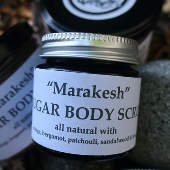 Jar of 'Marakesh' sugar body scrub with a white label on a textured surface.