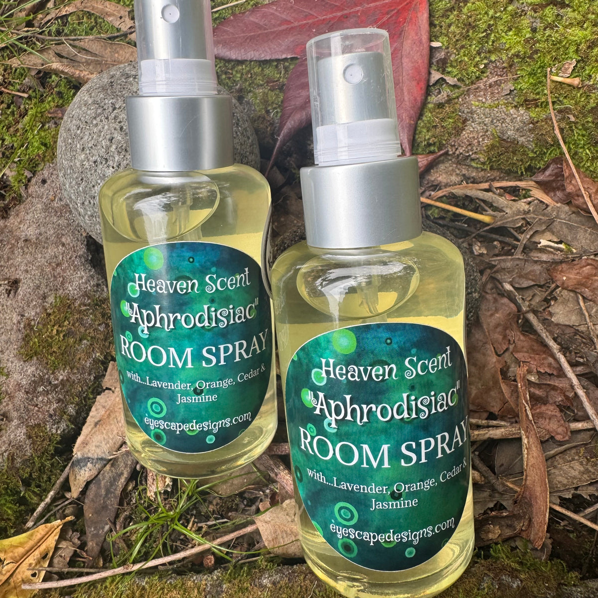 Two bottles of Heaven Scent Aphrodisiac Room Spray on a natural background with leaves and moss.