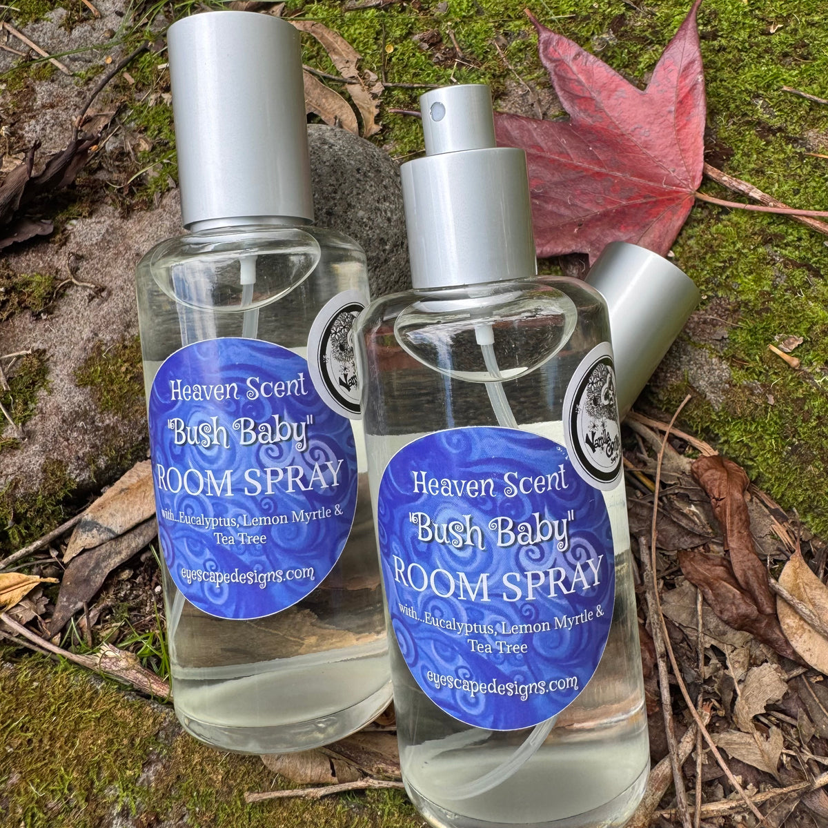 Two bottles of Heaven Scent 'Bush Baby' Room Spray on a natural background with leaves and moss.