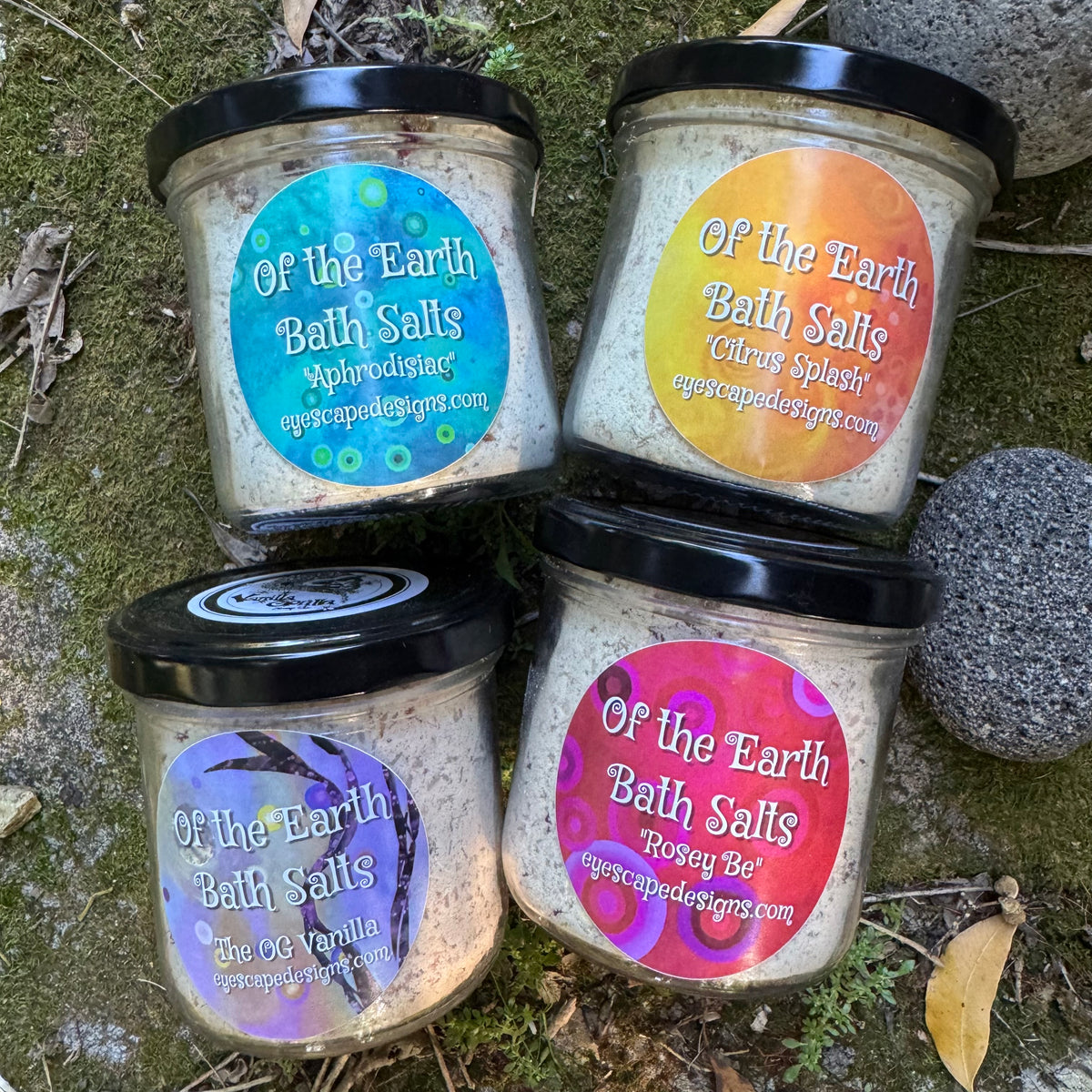 Four jars of 'Of the Earth Bath Salts' with colorful labels on a natural background.