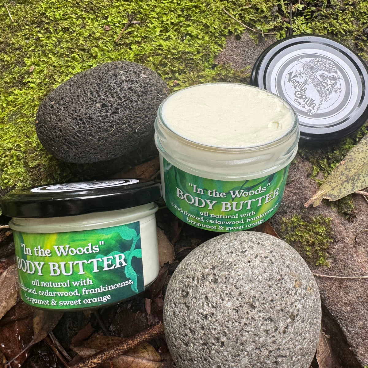 Two jars of 'In the Woods' body butter on a natural background with stones and moss.