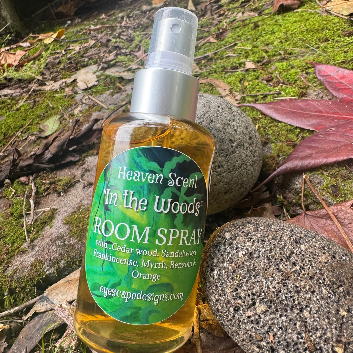 Room spray bottle labeled 'In the Woods' by Heaven Scent on a natural background with rocks and leaves.