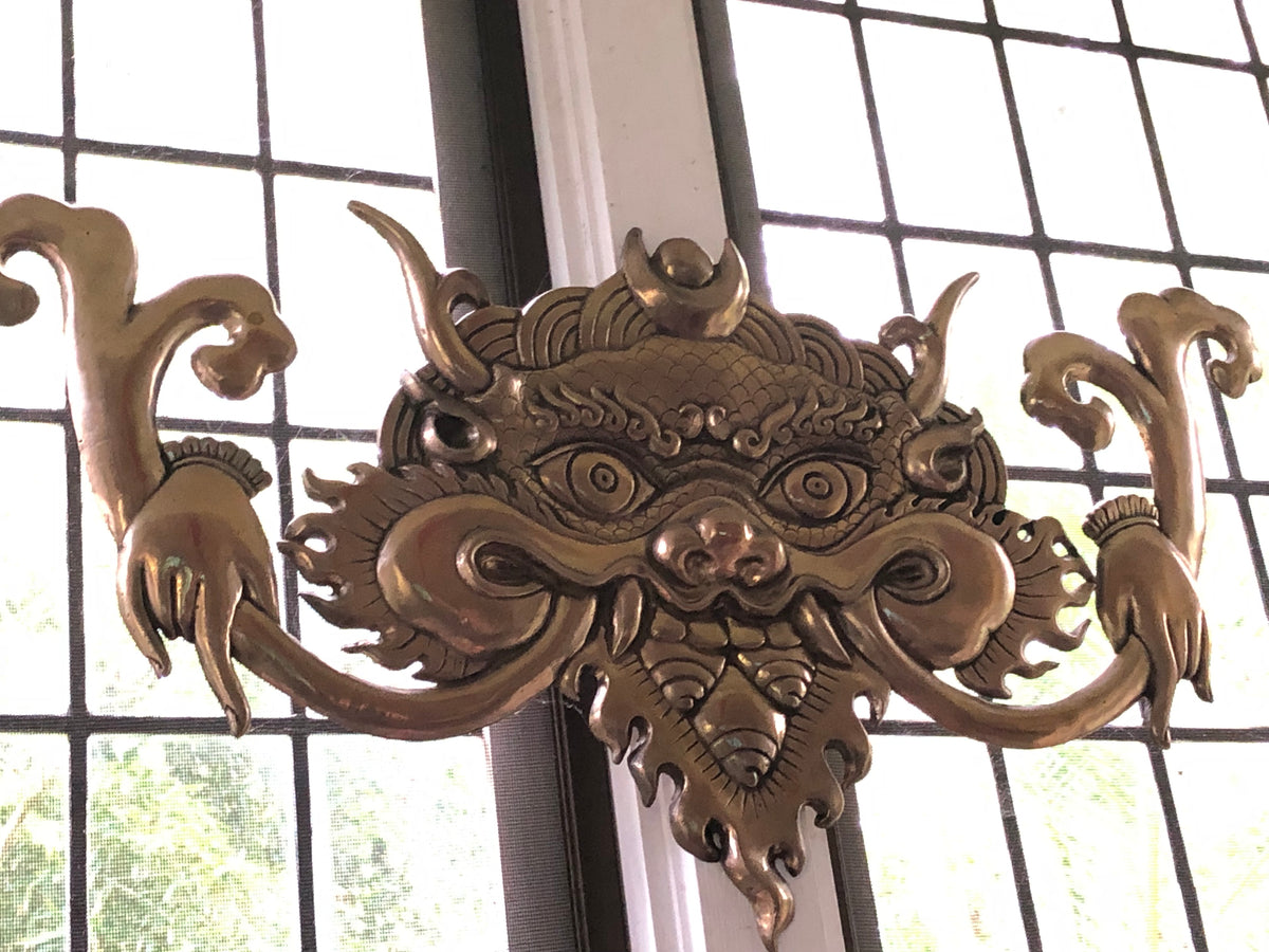 Shiny bronze wall hanging of khirtimukha on a washed out window
