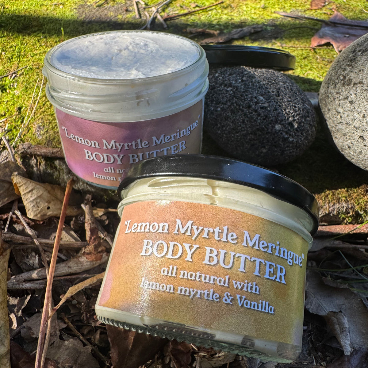 Two jars of Lemon Myrtle Meringue Body Butter on a natural background with rocks and leaves.