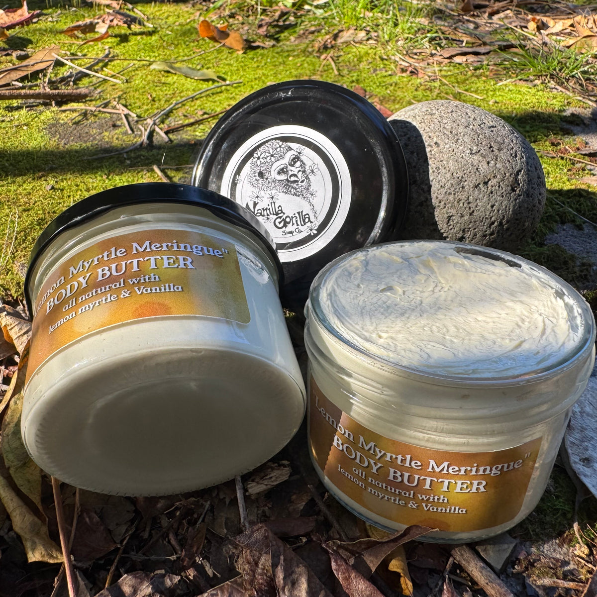 Three containers of Myrtle Meringue body butter on a natural background with leaves and stones.