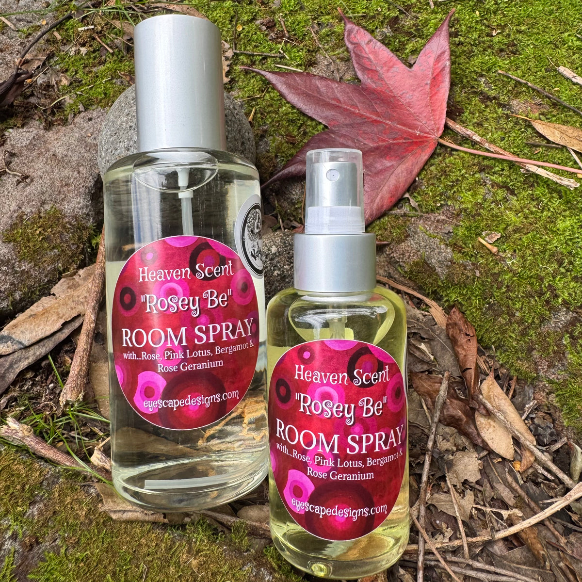 Two bottles of Heaven Scent 'Rosey Be' room spray on a natural background with leaves and moss.