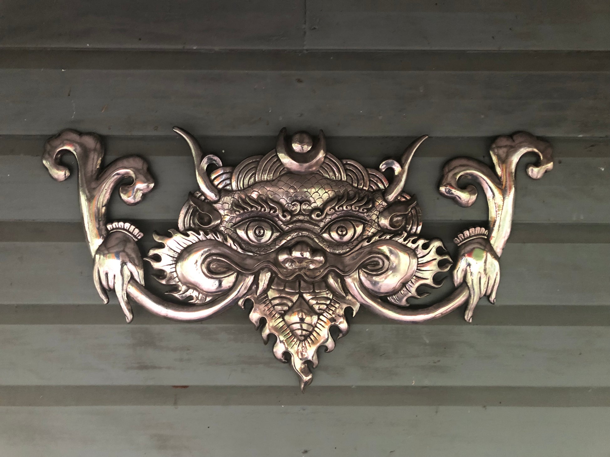 Shiny polished khirtimukha wall hanging on a khaki wall 