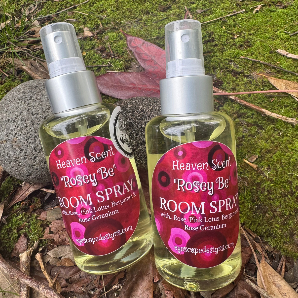 Two bottles of 'Heaven Scent Rosey Be' room spray on a natural background with moss and leaves.