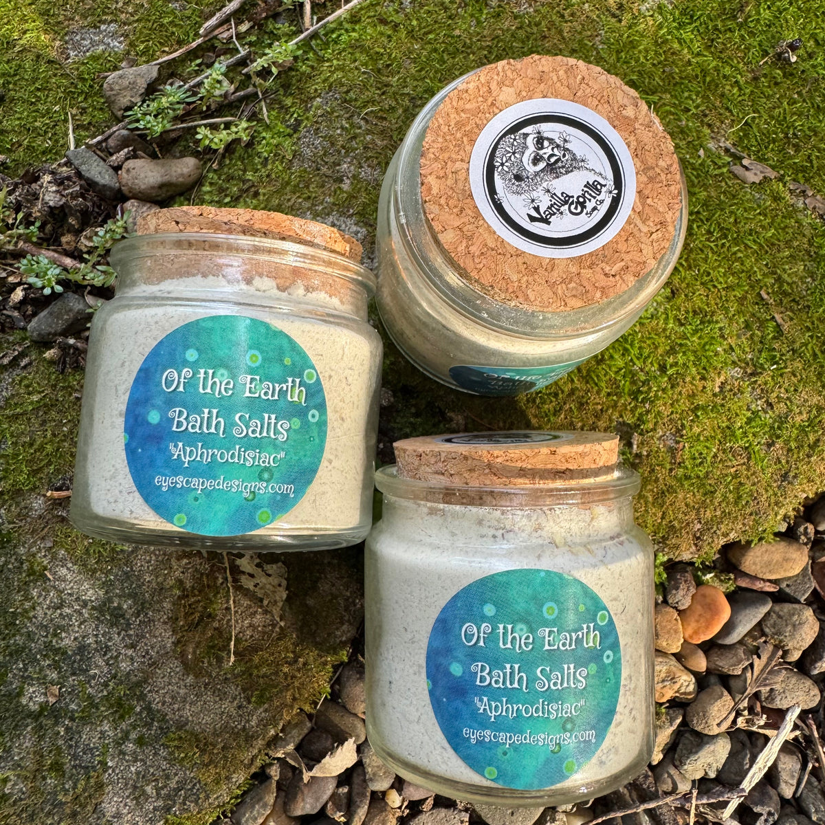 Three jars of 'Of the Earth Bath Salts Aphrodisiac ' on a natural background with moss and stones.