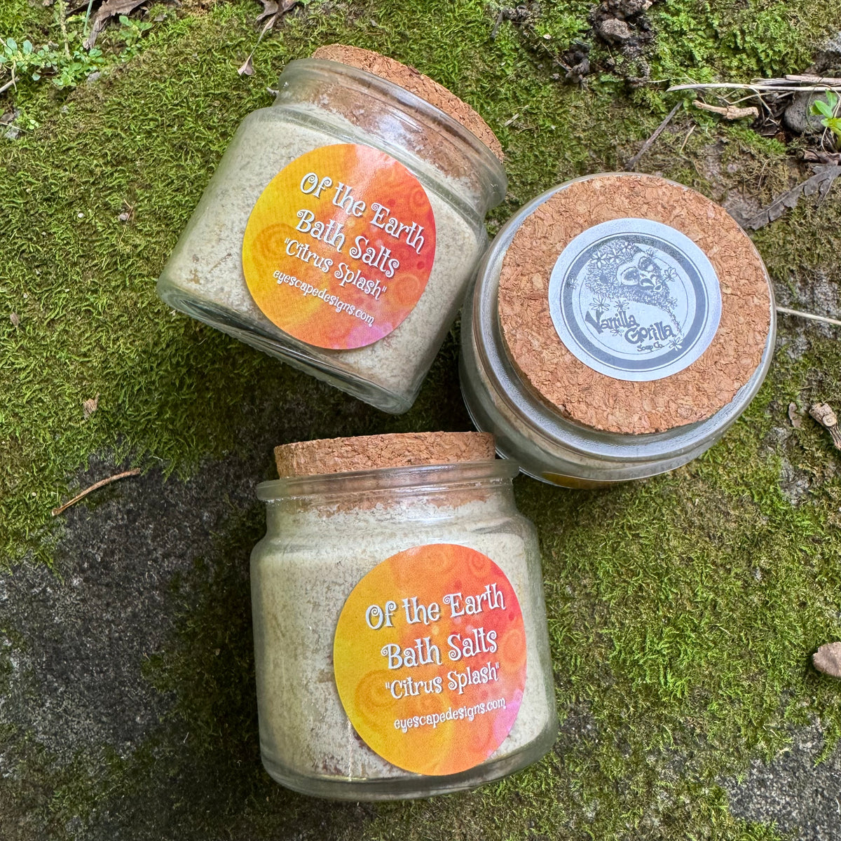 Three jars of 'Of the Earth Bath Salts' on a mossy surface