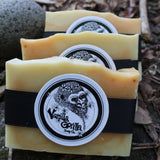 Three bars of lemon myrtle & tumeric soap with black ribbon vanilla gorilla labels on a stone surface