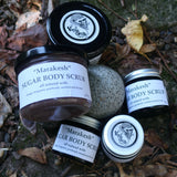 Jars of Marakesh Sugar Body Scrub on a natural stone surface with leaves.