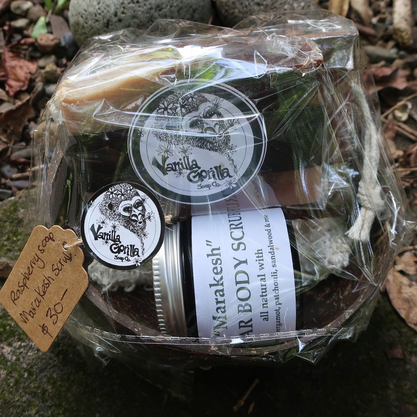 Jar of body scrub & raspberry soap on a wooden soap drainer & soap bag cello wrapped in a coconut bowl