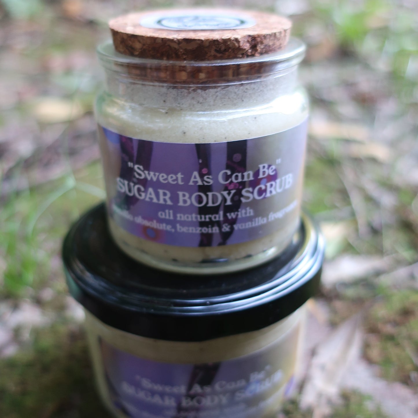 Jar of sweet as can be Vanilla body scrub with a purple label on a natural background