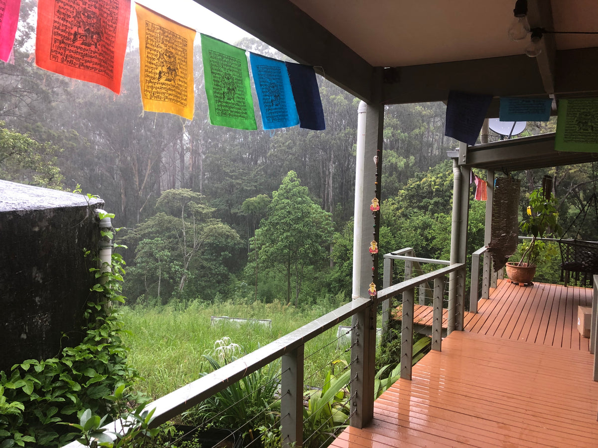 Rainbow prayer flags hanging on a verandah looking out to a wet bush land