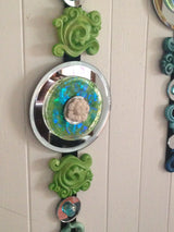 close up of green apple sculpted wall art dangle  w/ round mirror and white lotus